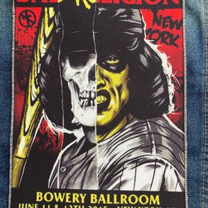 May include: A rectangular fabric patch featuring a split-face graphic of a skull and a person in a baseball uniform. The text reads BAD RELIGION, NEW YORK, and BOWERY BALLROOM JUNE 11 & 12TH 2015 - NEW YORK, NY. The design uses red, yellow, black, and white.