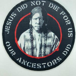 Puede incluir: Un parche bordado circular que presenta un retrato en blanco y negro de una persona indígena con el cabello trenzado. El texto "JESUS DID NOT DIE FOR US OUR ANCESTORS DID" está bordado en blanco alrededor del borde, rodeado por un círculo rojo.