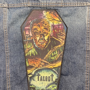 Pode incluir: Um remendo preto e branco em forma de caixão com uma ilustração de lobisomem. O lobisomem é retratado com uma expressão feroz, cercado por um cenário de floresta escura. O texto "TALBOT" está escrito em uma lápide em primeiro plano.