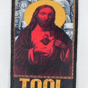 May include: A rectangular patch featuring a stylized image of Jesus with a red heart and a yellow halo. The word "TOOL" is printed in yellow at the bottom. The patch has a black border and a textured appearance.