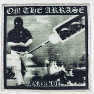 May include: A square fabric patch featuring a black and white graphic of a person wearing a mask, standing near a traffic light. The text "OI! THE ARRASE" is printed at the top, and "ANARKOI!" is printed at the bottom in a bold, white font.