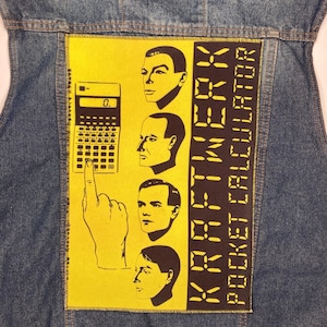 Puede incluir: Chaqueta vaquera azul con un parche amarillo. El parche muestra un gráfico de calculadora, cuatro caras estilizadas y el texto "KRAFTWERK POCKET CALCULATOR" en negro. La chaqueta es de mezclilla.