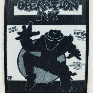 Könnte beinhalten: Schwarz-weißer Aufnäher mit dem Schriftzug "OPERATION IVY" im Graffiti-Stil. Der Aufnäher zeigt die Silhouette einer Person mit Hut. Der Text "CD OUT 11.06.07" ist ebenfalls sichtbar.
