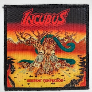 Könnte beinhalten: Ein schwarzer und roter gewebter Patch mit dem Bandnamen "Incubus" in roten Buchstaben und dem Albumtitel "Serpent Temptation" in weißen Buchstaben. Der Patch zeigt ein Bild von einem Baum mit einer Schlange, die sich um ihn herumwindet, und zwei Skeletten am Fuß des Baumes.