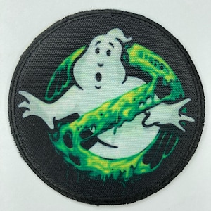 Op de afbeelding: Een ronde zwarte patch met een witte geest en groene slijm in de vorm van een verbodssymbool. De geest heeft een verbaasde uitdrukking en is omringd door druipende groene slijm.