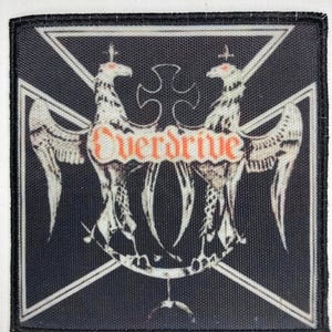 May include: Black and white embroidered patch with a black cross and two white birds with outstretched wings. The word "Overdrive" is written in orange letters across the center of the patch.