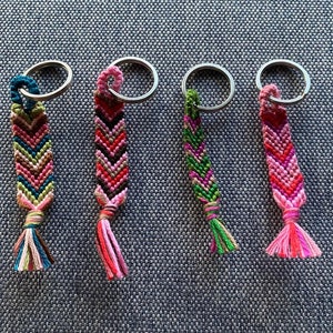 Può includere: Quattro braccialetti dell'amicizia colorati con anelli portachiavi. I braccialetti sono realizzati con filo rosa, verde, blu e nero. I braccialetti sono legati in un motivo a chevron.