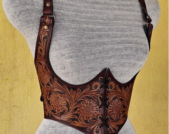 May include: A brown leather corset with floral tooling and a black lace-up front. The corset has adjustable straps and a back closure.