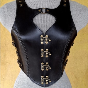 May include: A black leather corset with a heart-shaped cutout in the front. The corset has a series of decorative brass buckles down the front.