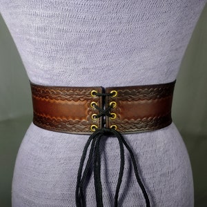 May include: A brown leather corset belt with a lace-up closure and gold eyelets. The belt has a decorative embossed pattern.