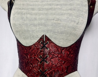 May include: A red leather corset with a floral embossed design and black lacing. The corset has adjustable straps and a pointed bottom.
