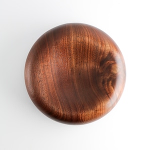 May include: A circular wooden bowl, featuring a deep brown hue and prominent wood grain patterns. The bowl has a smooth, polished surface and a simple design. It is likely intended for serving or decorative purposes.