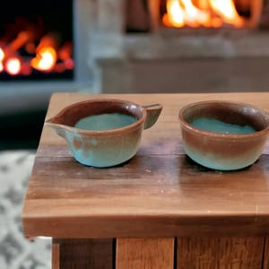 May include: Two small ceramic vessels with a two-tone finish. The exterior and interior feature a smooth, matte brown glaze on the upper portion and a textured, light turquoise blue glaze on the lower portion. One vessel includes a small pouring spout.