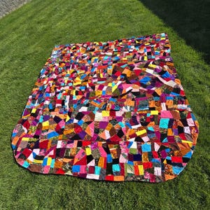 May include: A large rectangular quilt constructed from a multitude of small, irregularly shaped fabric patches in a vibrant array of colors including red, blue, yellow, pink, purple, green, and black, featuring various textures and patterns.