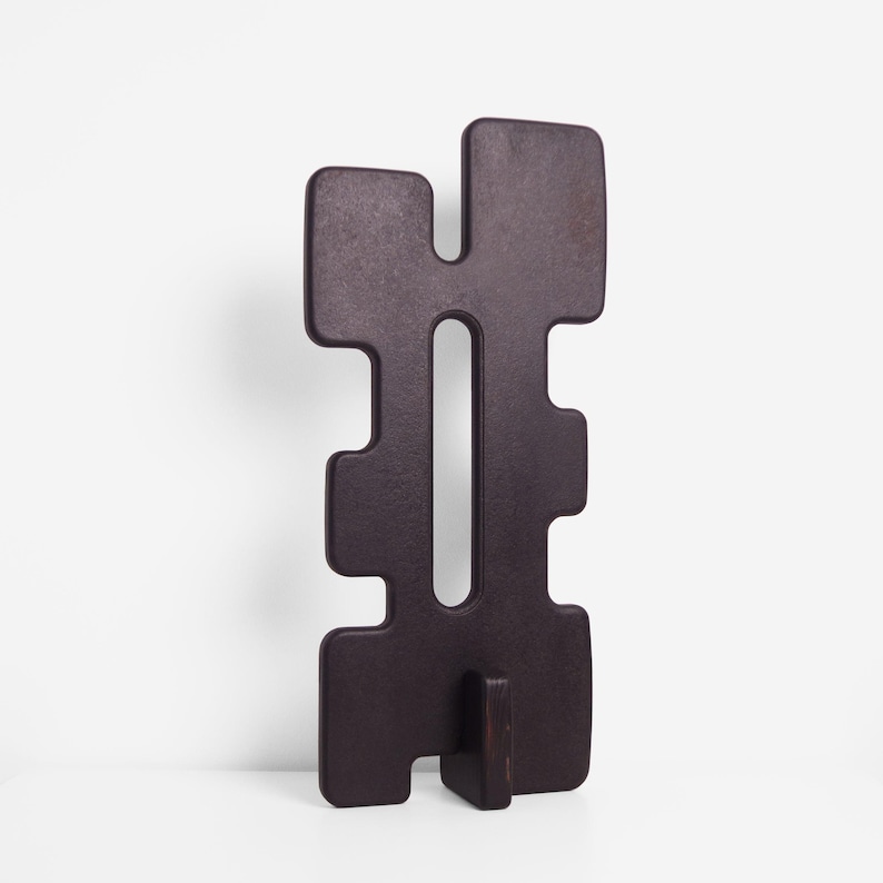 Image of the TREZE sculpture in matte black, shown slightly turned to the side to reveal its geometric contours and the elongated central cutout. The sculpture stands upright on its matching matte black base, placed on a clean white surface against a plain white background.