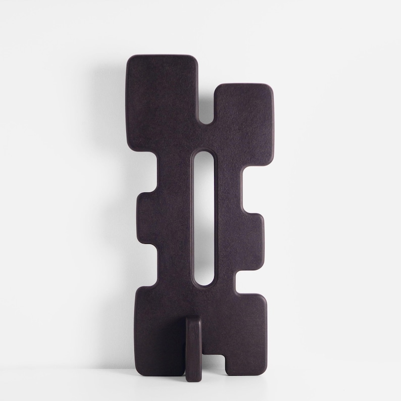 Tall black sculpture with abstract shape and very subtle maroon undertones. The modern sculpture is standing on a white background.