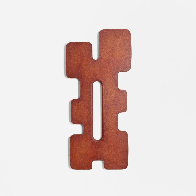 Close‑up of an abstract wall sculpture in red hues with a geometric, symmetrical shape and central vertical opening. The textured surface and sculptural form highlight modern handcrafted wall art ideal for contemporary home decor.