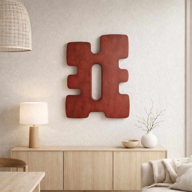 Minimalist Nordic interior featuring a large red abstract wooden sculpture mounted on a light textured wall above a pale wood sideboard, illuminated by soft natural light and warm tones.