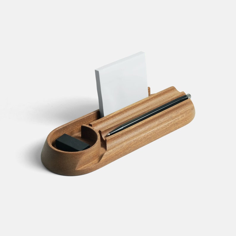 A light brown wooden desk organizer with a post-it pad and two pens in its compartments.