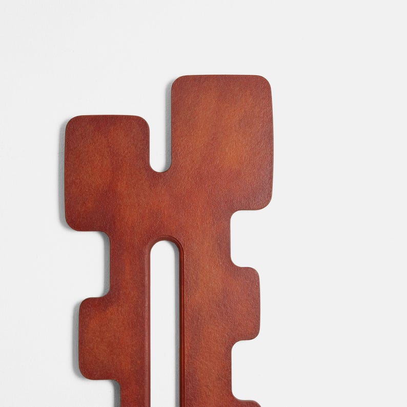 Close‑up of an abstract wall sculpture in red hues with a geometric, symmetrical shape and central vertical opening. The textured surface and sculptural form highlight modern handcrafted wall art ideal for contemporary home decor.