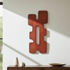 Abstract red wall sculpture in a modern minimalist interior, displayed above a wooden sideboard with ceramic vases. Contemporary wall art in red hues illuminated by natural light from large windows, ideal for modern home decor and statement art pieces.