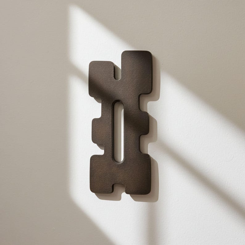 Reddish-brown abstract wall sculpture with geometric cutouts, vertically mounted above a mid-century modern wooden sideboard. Handcrafted contemporary art piece in a minimalist interior with ceramic vases, greenery, and city view. Ideal for modern apartments, curated design spaces, or art-focused interiors.