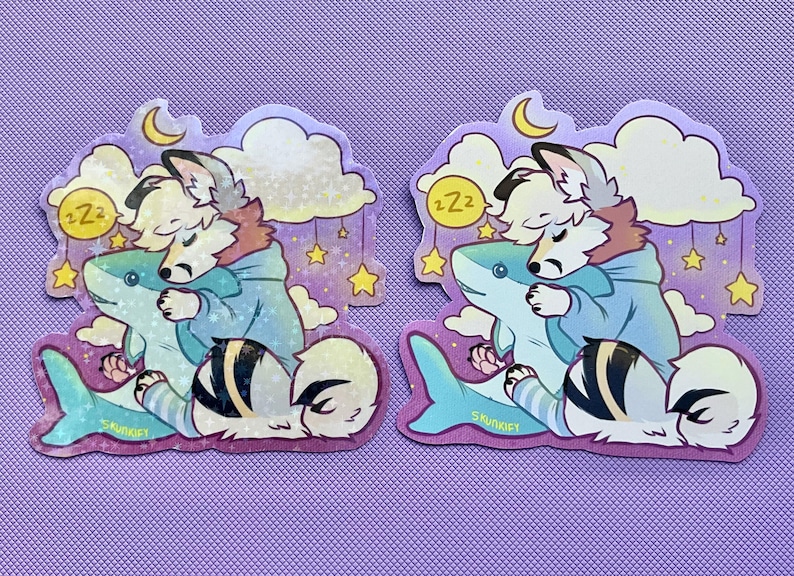 May include: Two identical die-cut stickers featuring a white and grey anthropomorphic canine character with a blue hoodie, sleeping while hugging a light blue shark plush. The background includes yellow stars, clouds, a crescent moon, and Zzz text.