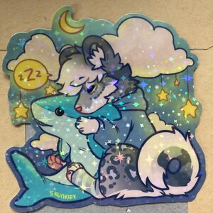 May include: A holographic sticker featuring a gray and white wolf-like creature with a spotted tail hugging a blue shark plush toy. The scene includes a yellow crescent moon, clouds, and hanging stars against a dark teal background with the text Skunkify.