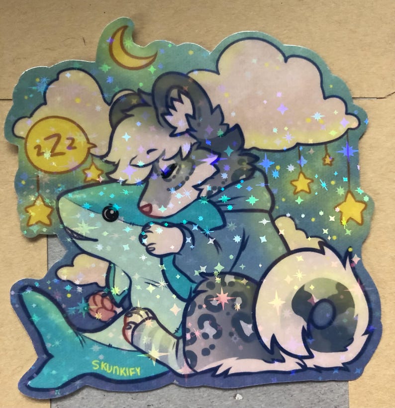 May include: A holographic sticker featuring a gray and white wolf-like creature with a spotted tail hugging a blue shark plush toy. The scene includes a yellow crescent moon, clouds, and hanging stars against a dark teal background with the text Skunkify.