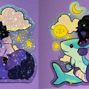 May include: A holographic sticker featuring a dark purple and black creature wearing a light purple hoodie, hugging a light blue shark. The background includes yellow clouds, a crescent moon, hanging stars, and a yellow circle with Zz text.