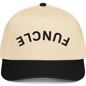 May include: A beige baseball cap with a black brim and a black button on top. The word "FUNCLE" is embroidered in black, arched across the front of the cap.