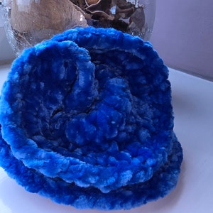 Könnte beinhalten: Ein leuchtend blauer, plüschiger, gehäkelter Hut. Der Hut besteht aus einem weichen, strukturierten Material und hat ein mehrschichtiges Design. Der Hut liegt auf einer weißen Oberfläche.