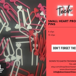 May include: A close-up of a pile of small heart-shaped prop pins. The pins are available in white and pink. The image includes the text "DTE Tech", "Small Heart Prop Pins", "5 clips $2.00", "10 clips $3.50", "Don't Forget Them!" and "Down to Earth Technologies".