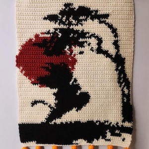 Puede incluir: Un tapiz de pared de ganchillo de color crema con un diseño de árbol negro y rojo. El árbol se encuentra sobre un fondo crema, con una base negra y borlas naranjas con detalles en marrón y blanco en la parte inferior. Una barra de madera roja en la parte superior.