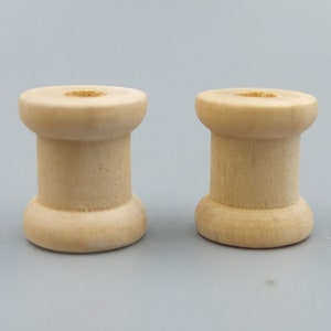 May include: Two wooden spools, each with a smooth, light brown finish. The spools are cylindrical with a slightly raised lip around the top and bottom.