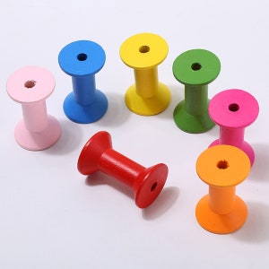 May include: Seven wooden spools in different colors: pink, blue, yellow, green, red, orange, and fuchsia. The spools are all the same size and shape, and they have a hole in the center.