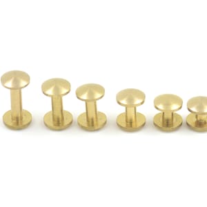 May include: A set of six brass rivets in various sizes. The rivets are round with a domed top and a flat base. They are arranged in a row from largest to smallest.