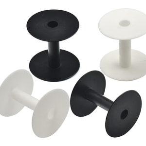 May include: Four plastic spools for thread or yarn. Two are black and two are white. The spools have a center hole and two flat circular ends.