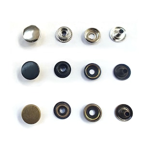 Puede incluir: Surtido de botones a presión metálicos en acabados plateado, negro y latón. Los botones a presión están en varias etapas de montaje, incluyendo la tapa, el casquillo y el perno.