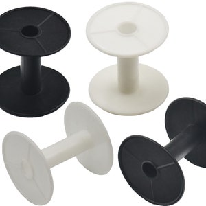 May include: A collection of black and white plastic spools. Each spool has a cylindrical center and two flat, circular ends. The spools are designed with a central hole and radial lines on the ends.