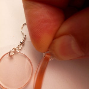 Pu&ograve; includere: Un paio di orecchini con un pendente ovale rosa chiaro e un pendente sottile, marrone e curvo.