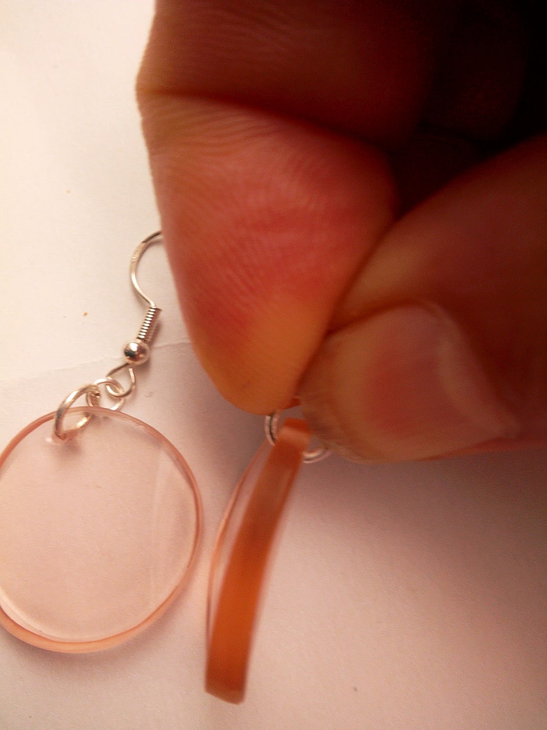 Pu&ograve; includere: Un paio di orecchini con un pendente ovale rosa chiaro e un pendente sottile, marrone e curvo.