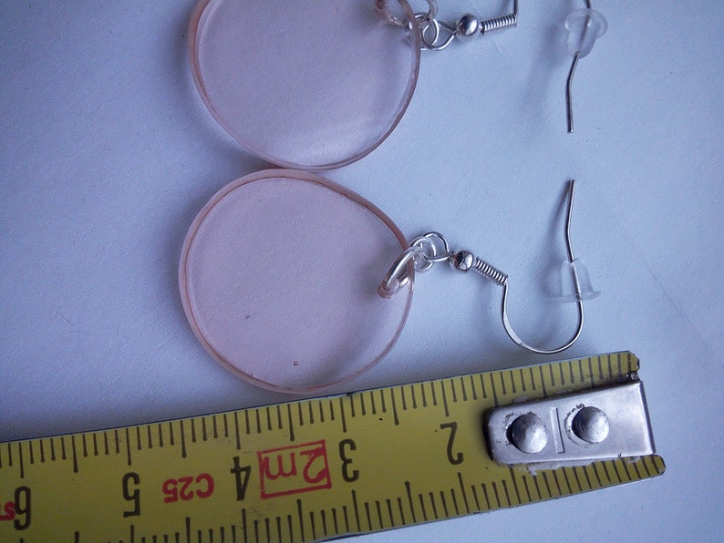 Pu&ograve; includere: Un paio di orecchini rotondi in acrilico rosa con ganci argentati. Gli orecchini hanno un diametro di circa 3 cm.