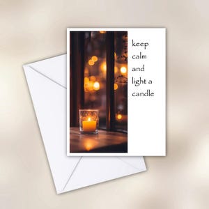 May include: A greeting card with the text "keep calm and light a candle" next to an image of a lit candle in a glass holder. The candle sits on a wooden surface near a window with blurred lights in the background. A white envelope is in the foreground.