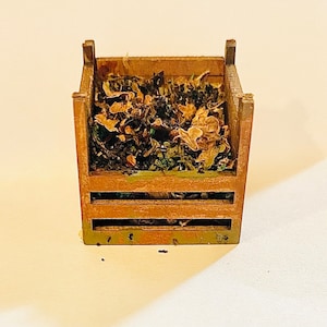 Puede incluir: Una pequeña caja de madera llena de hojas y ramitas secas. La caja tiene un acabado rústico marrón y está hecha de madera.