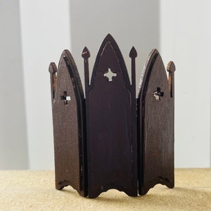 May include: A dark brown wooden room divider with a gothic design. The divider is made of four panels, each with a pointed arch and a cross-shaped cutout. The divider is standing on a light brown surface.