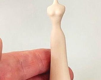 May include: A small, smooth, pale beige figurine shaped like a stylized human torso and dress. The object features a slender neck, defined chest area, and a long, tapered skirt that widens toward the base, creating a continuous, minimalist silhouette.