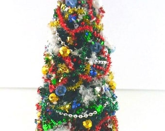 Könnte beinhalten: Ein Miniatur-Weihnachtsbaum aus grünem Lametta, verziert mit rotem und goldenem Lametta, weißem Kunstschnee und verschiedenen bunten Perlen. Der Baum ist mit einem silbernen Stern gekrönt und steht auf einem runden roten Sockel mit Goldrand.