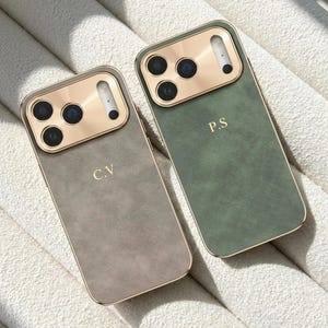 May include: Two smartphone cases with a textured matte finish, one in taupe and one in sage green. Each case features a metallic gold camera housing and gold-colored lettering, with the initials C.V on the taupe case and P.S on the green case.