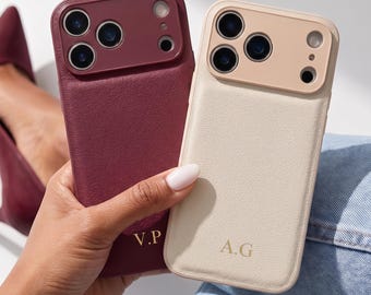 May include: Two rectangular smartphone cases with a textured leather-like finish. One case is deep burgundy with gold initials V.P, and the other is cream with gold initials A.G. Both feature a raised camera cutout frame matching their respective colors.